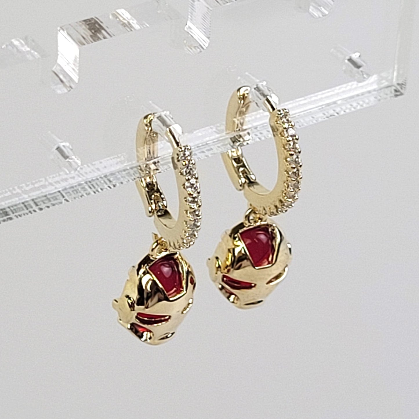 Gold hoop earrings with red gemstones on a clear stand.