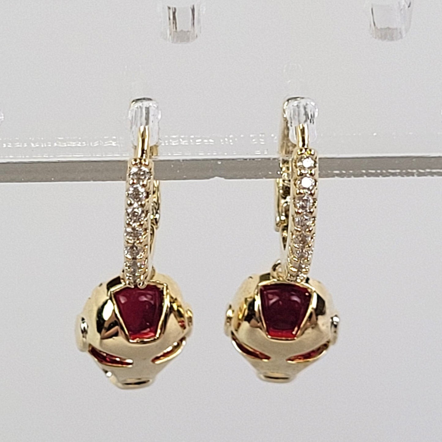 Gold earrings with red gemstones on a clear stand