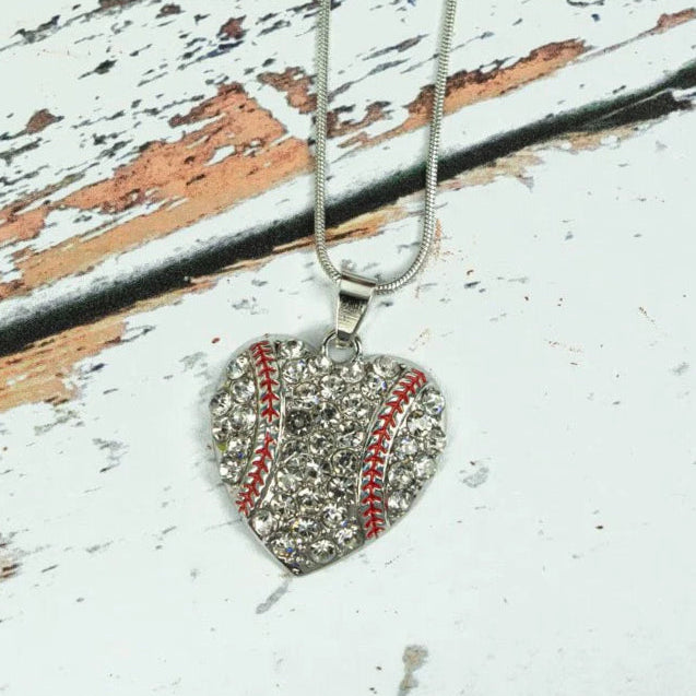 A heart-shaped baseball rhinestone pendant necklace with a silver tone and red highlights, displayed on a wooden surface.
