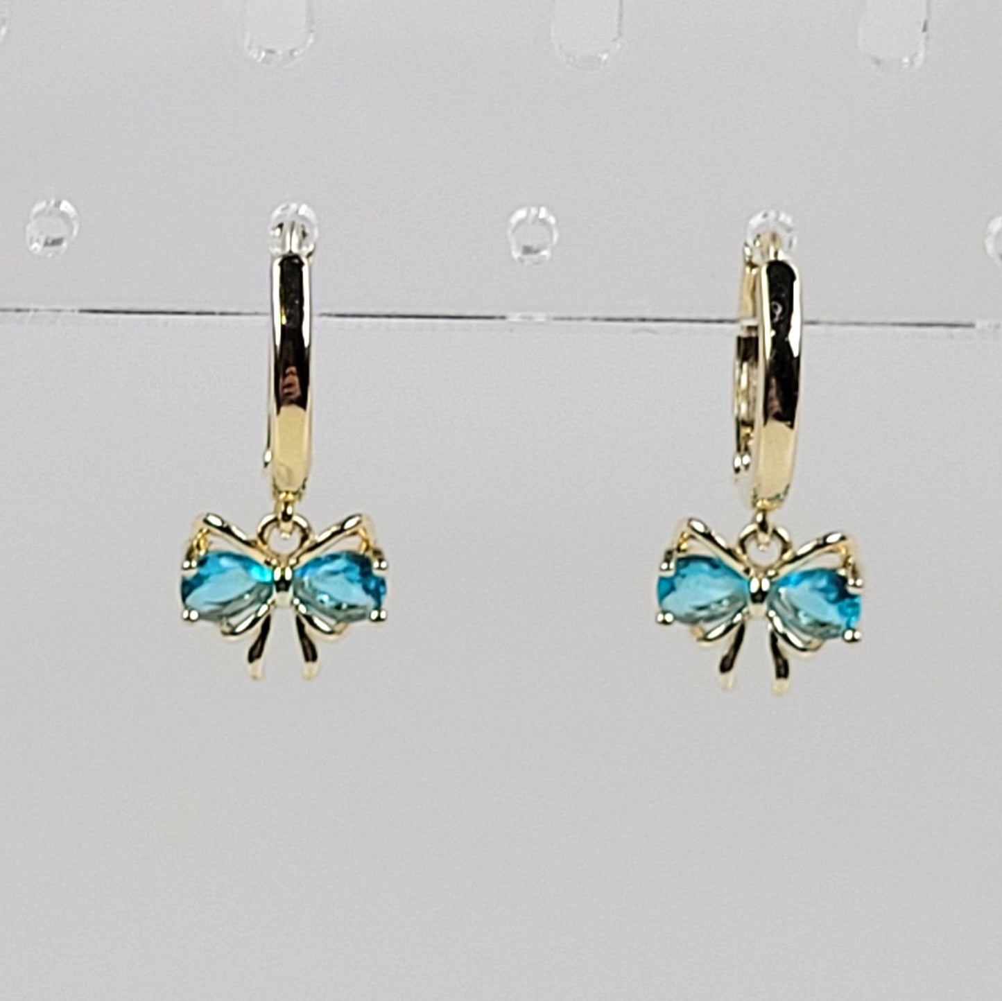 Gold bow earrings with blue gemstones on a gray background