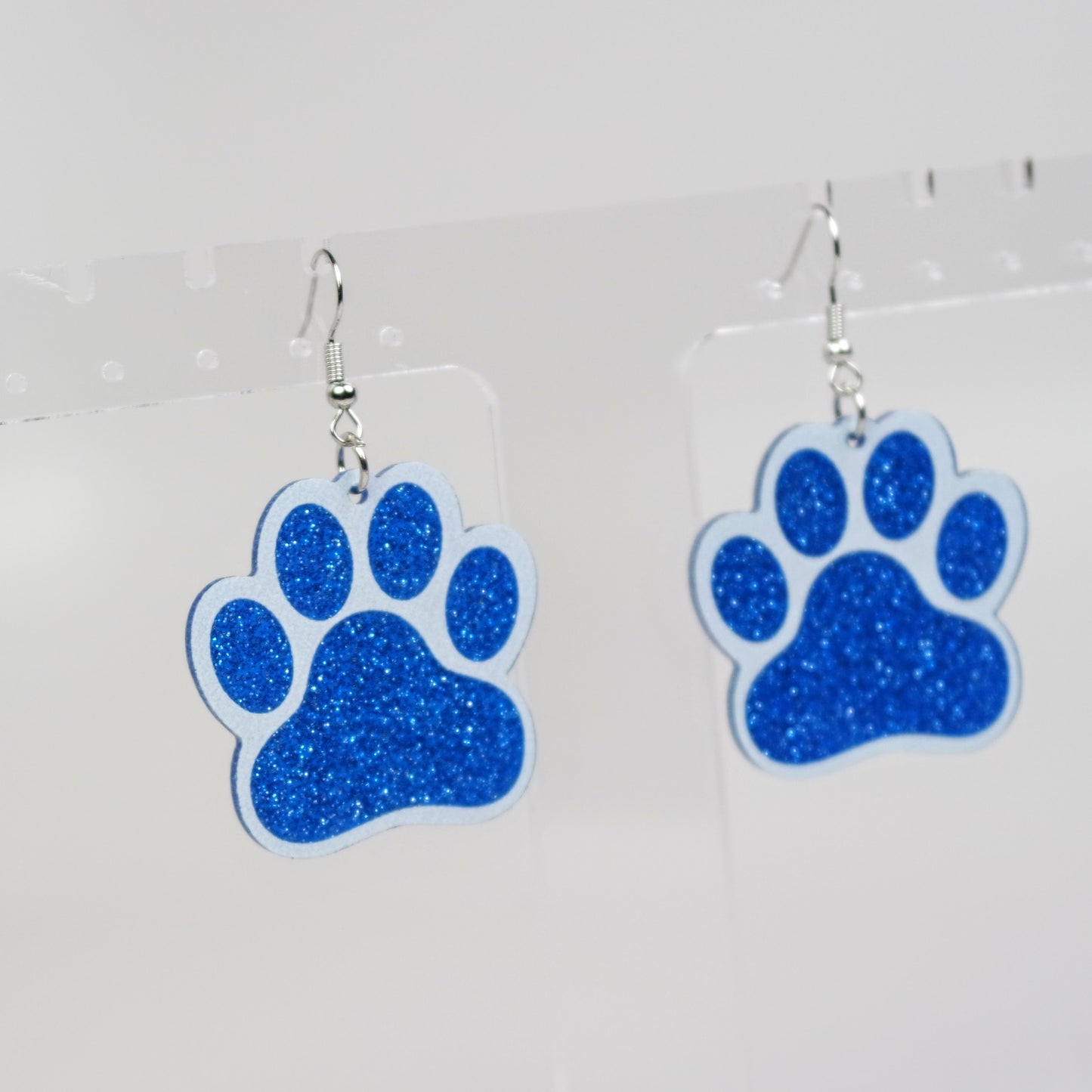 Blue glitter paw print earrings on a white background