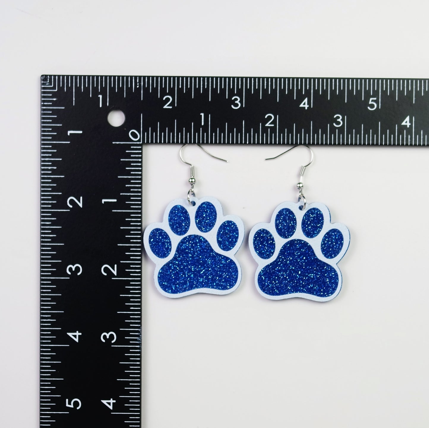 Blue glitter paw print earrings next to a ruler on a white background