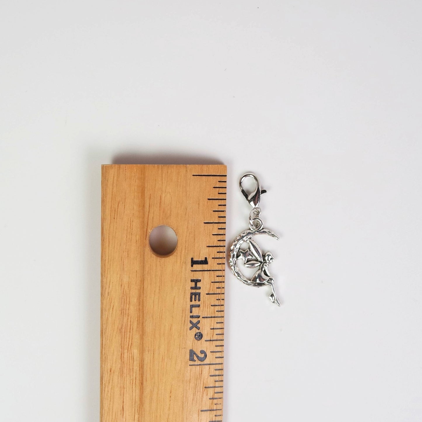 Silver charm on a wooden ruler for size reference