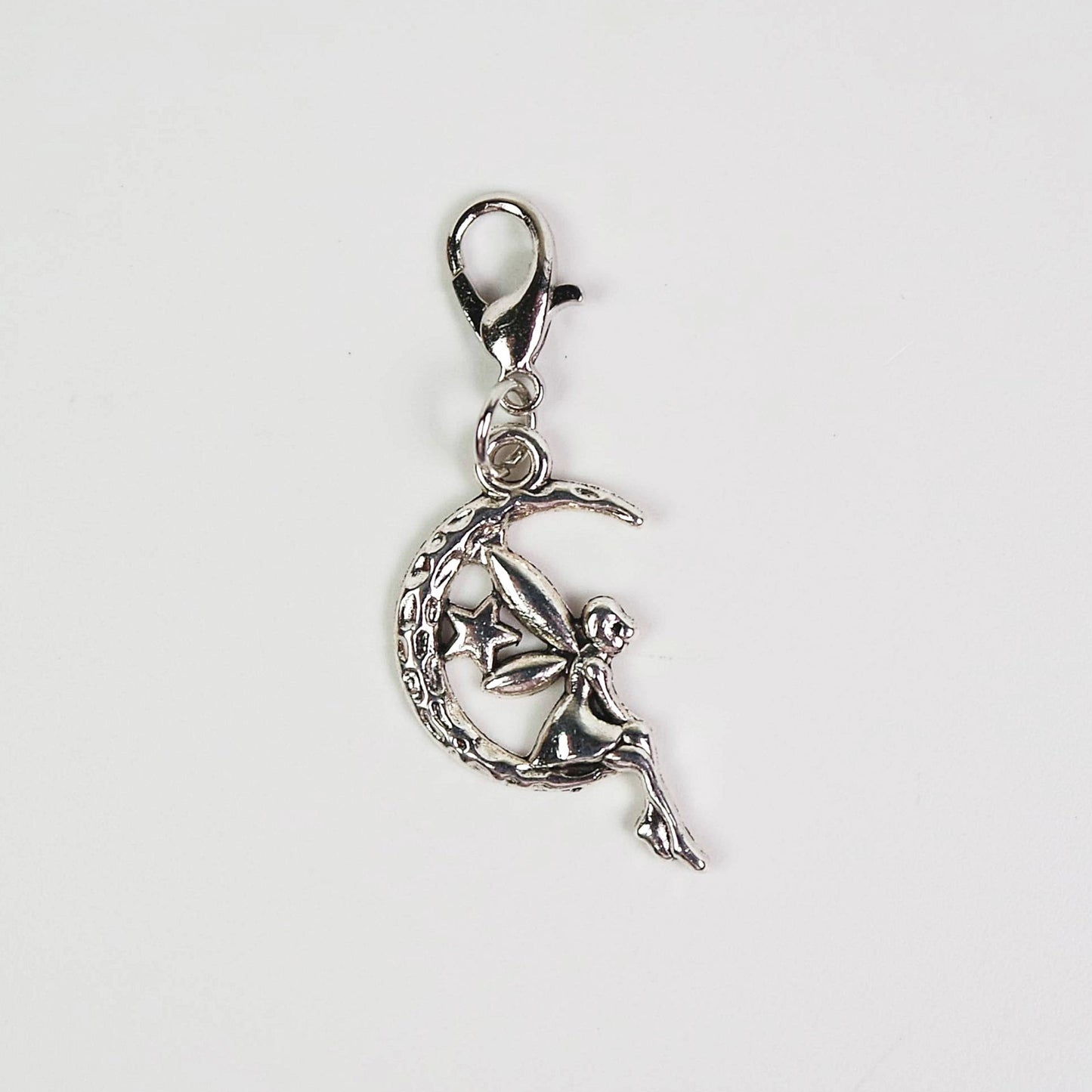 Silver fairy charm on a moon with a star, attached to a lobster clasp on a white background.