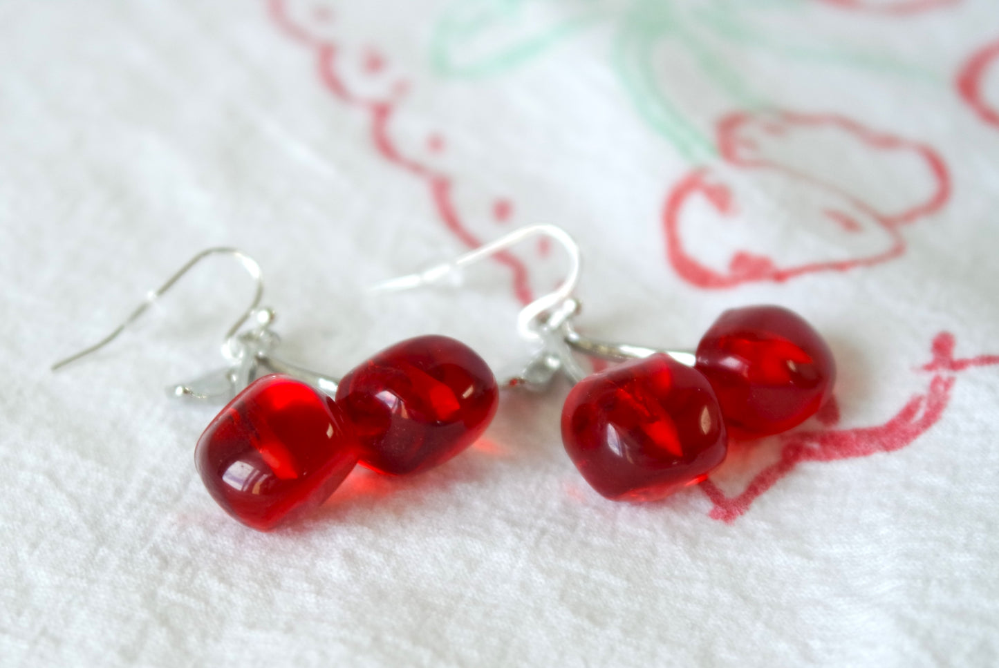 A pair of dangle earrings shaped like cherries with red and silver colors.