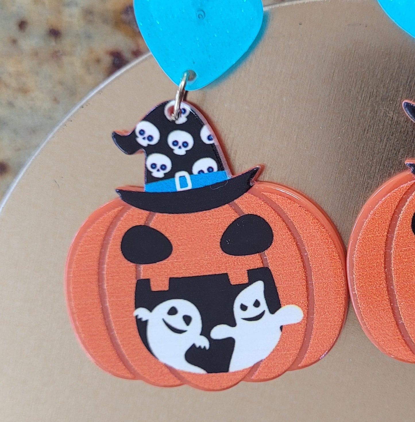 Halloween-themed pumpkin earrings with ghost design on a beige background
