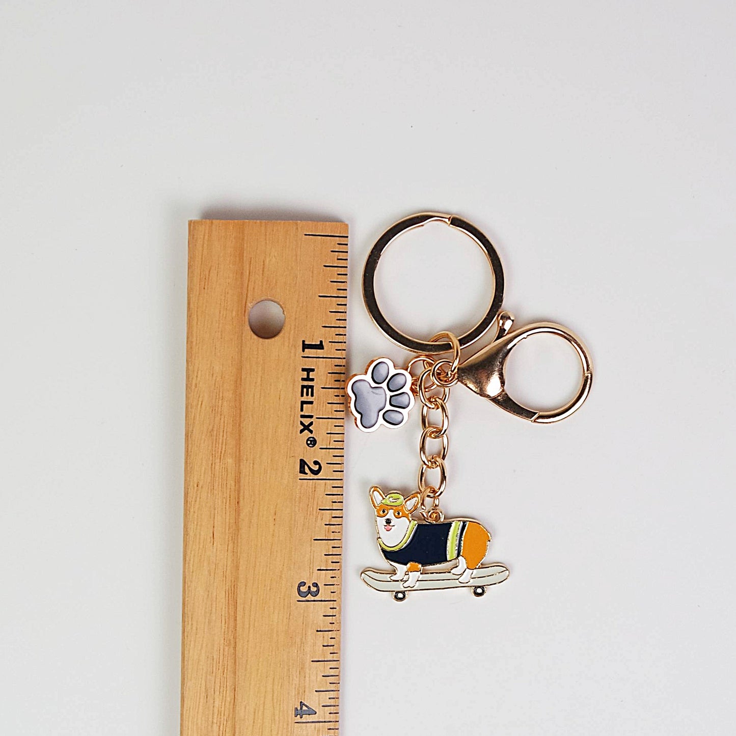 Keychain with a dog design and paw charm next to a ruler for scale on a light gray background