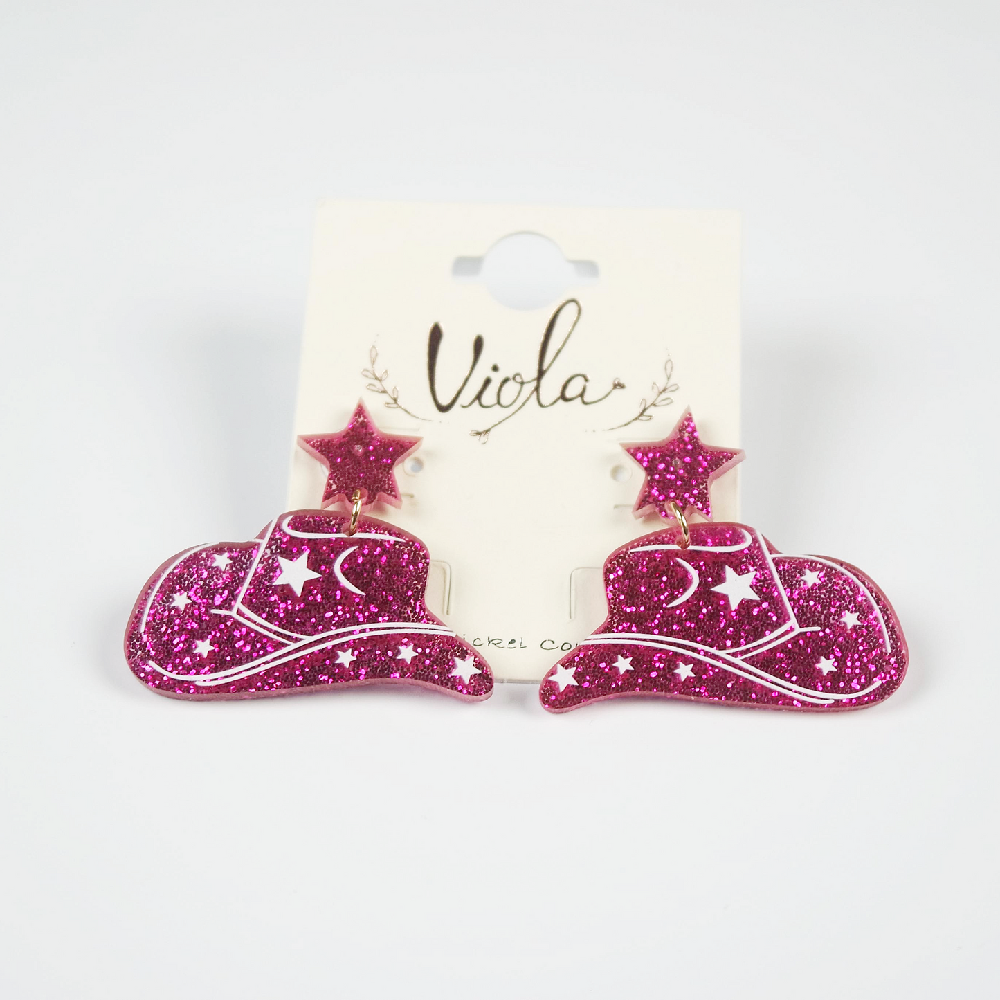Pink glittery cowboy hat earrings on a 'Viola' branded card against a white background