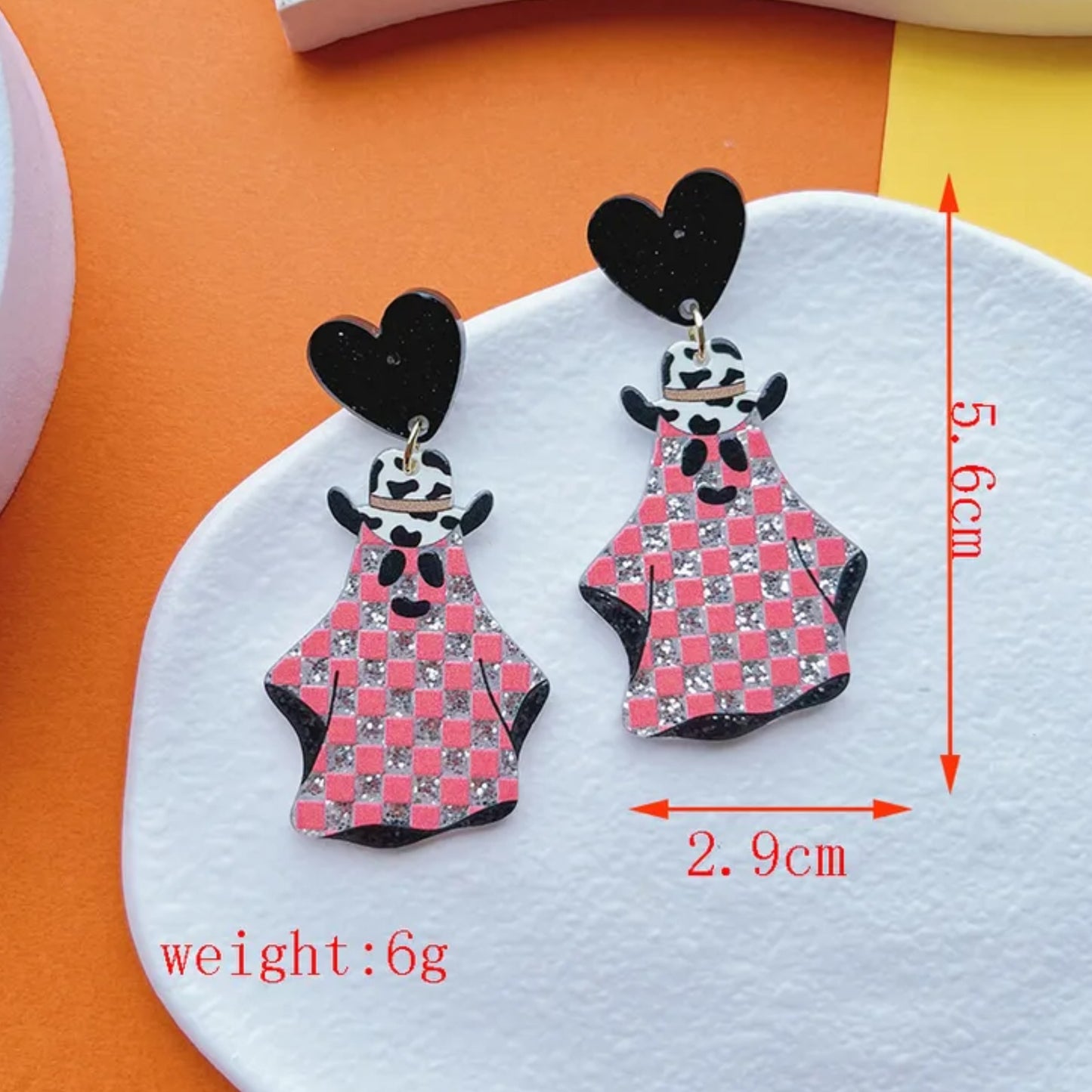 Pair of earrings with cartoon ghost cowgirl design on a white and orange background