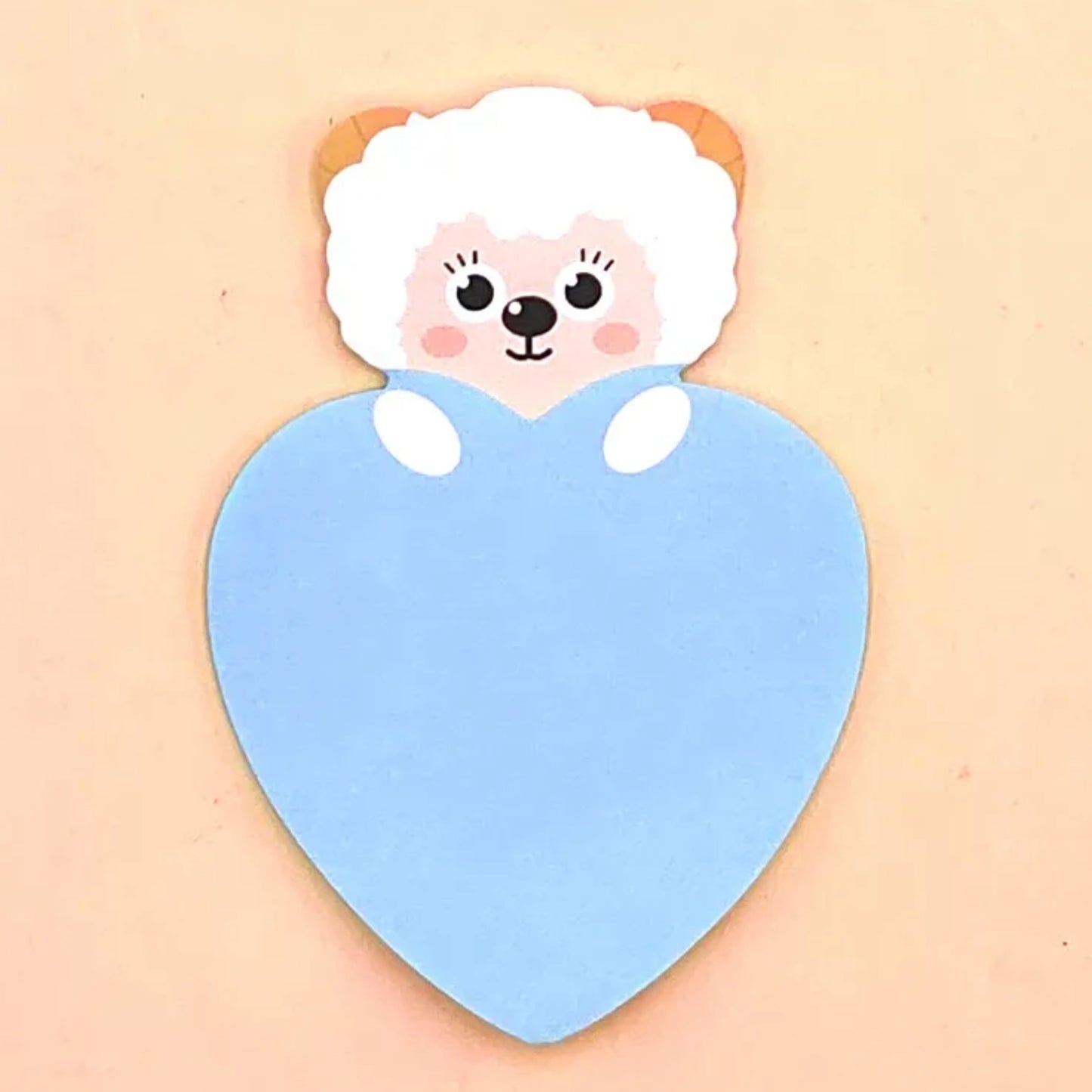 A heart-shaped blue sticky notepad with a cartoon lamb design on the top, presented against a plain background.