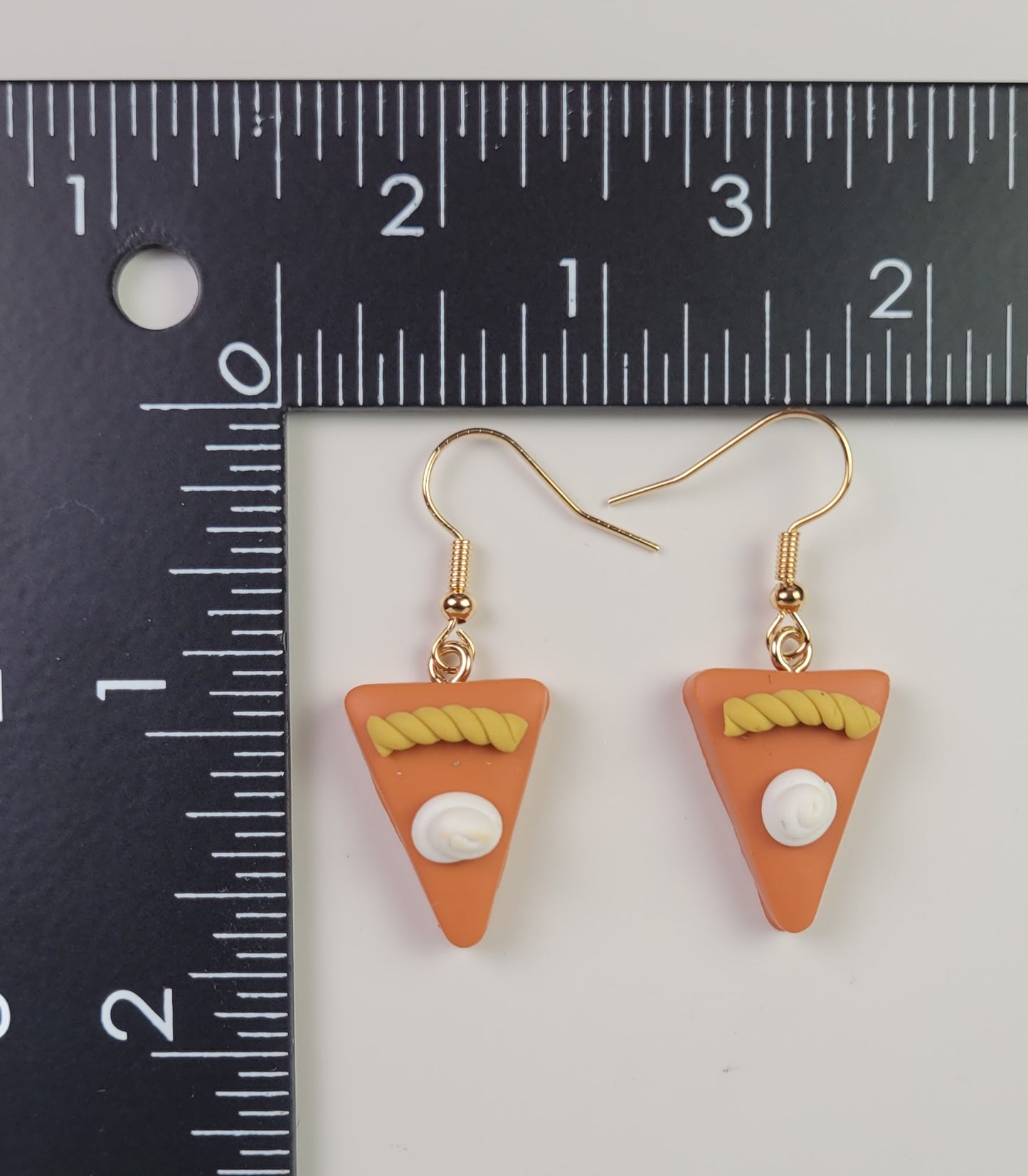 Triangular earrings with white centers and gold accents on a ruler for scale.