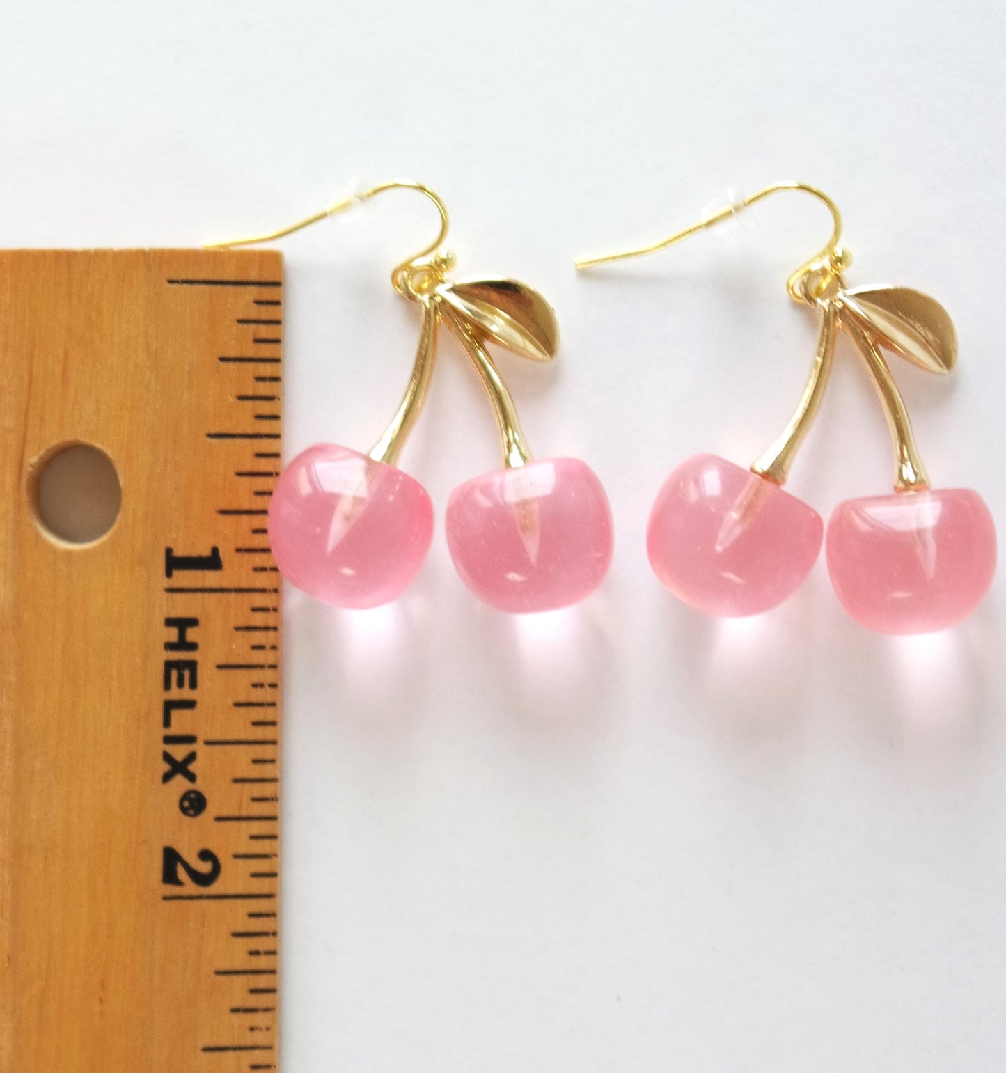 A pair of dangle earrings shaped like cherries with pink and gold.