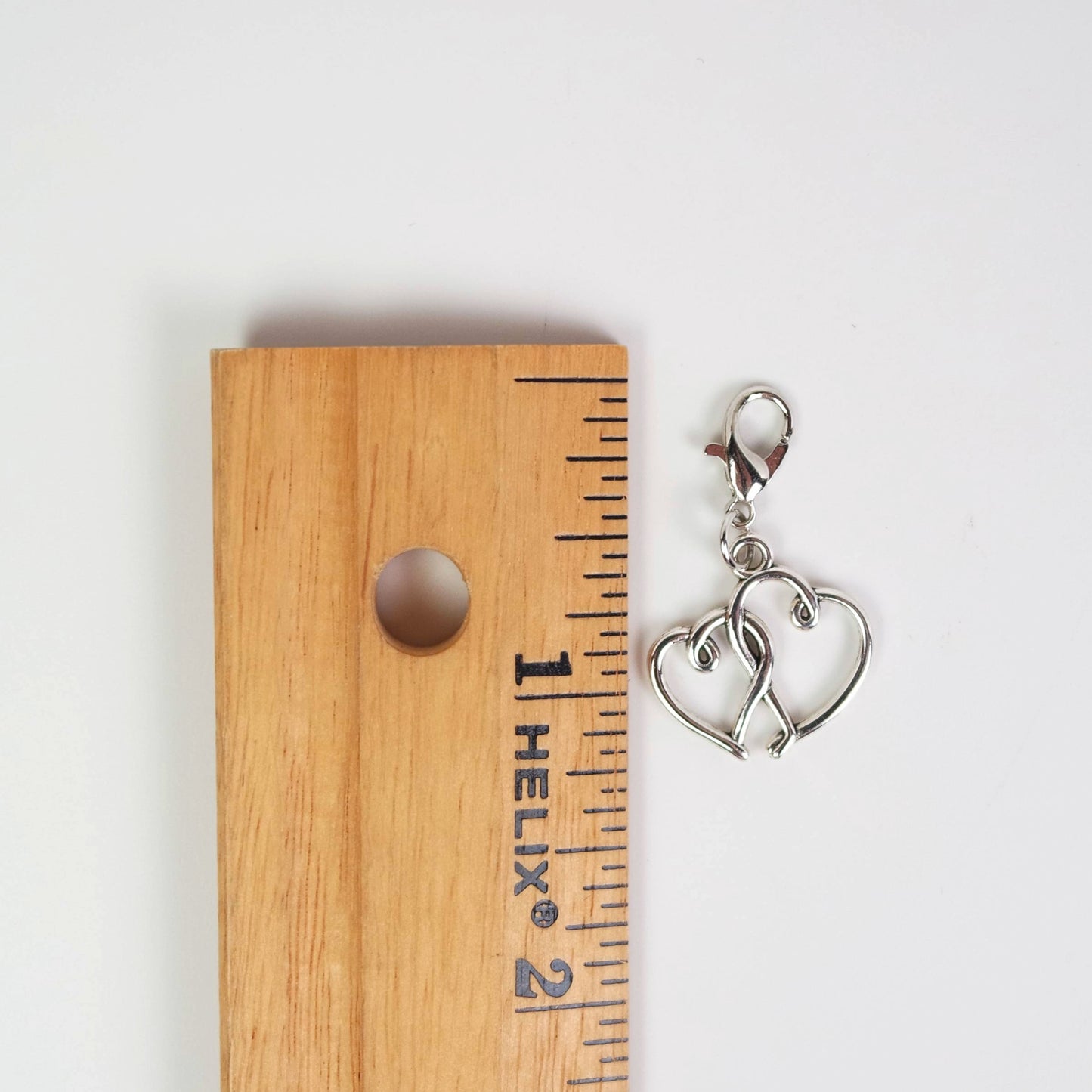 Silver heart-shaped charm on a wooden ruler for scale