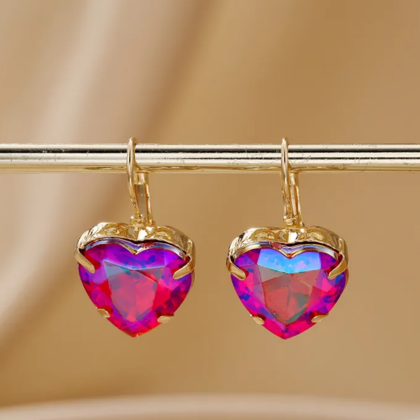 Heart-shaped earrings with colorful gemstones on a beige background