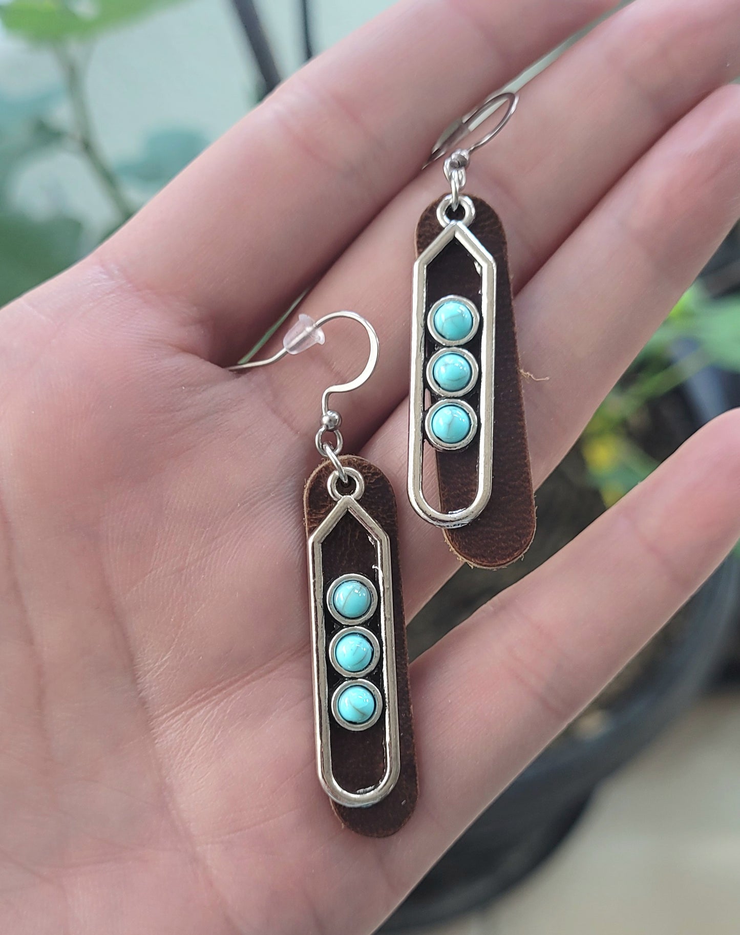 Pair of earrings with turquoise stones held in a hand against a blurred natural background