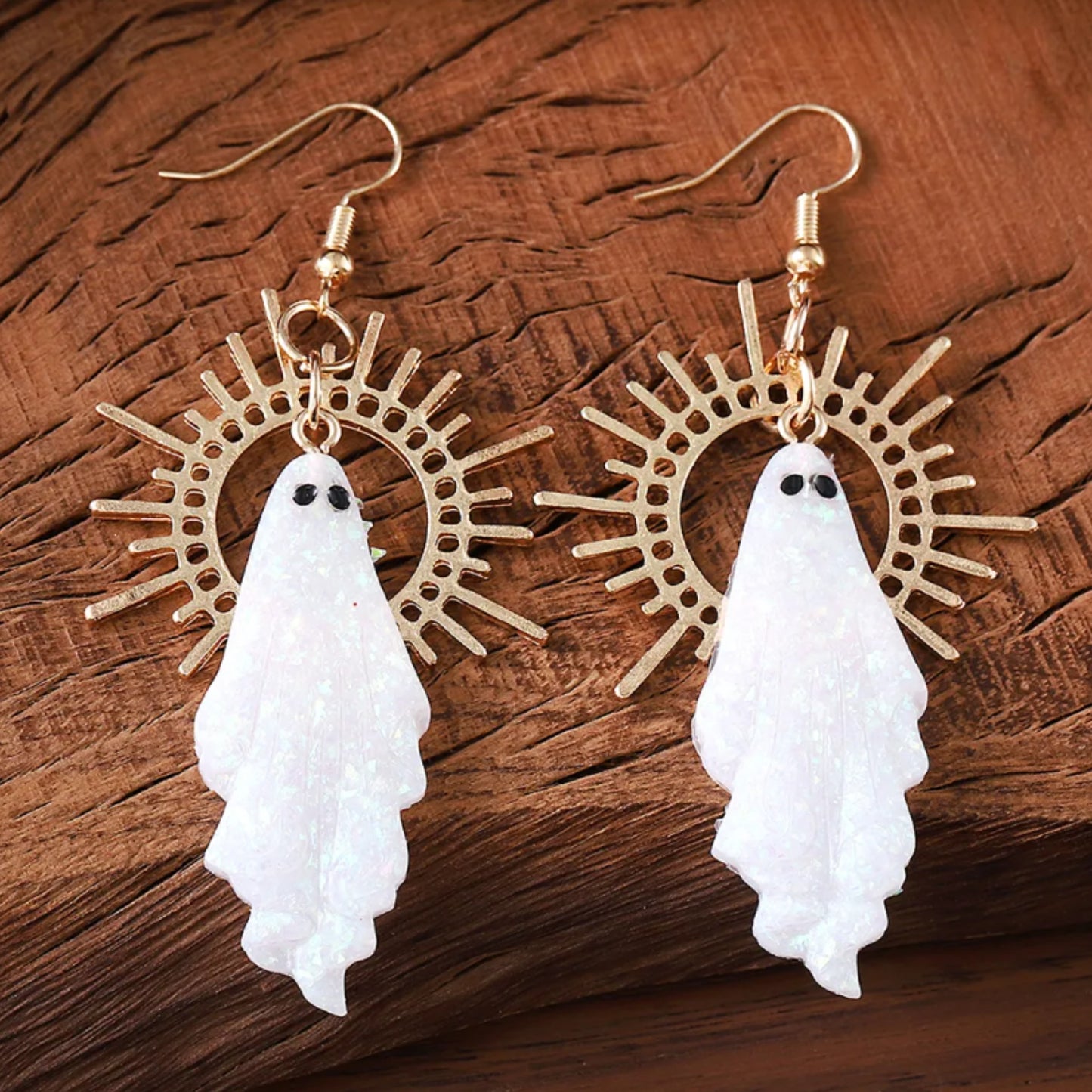 Ghost-shaped earrings with gold circular designs on a wooden surface
