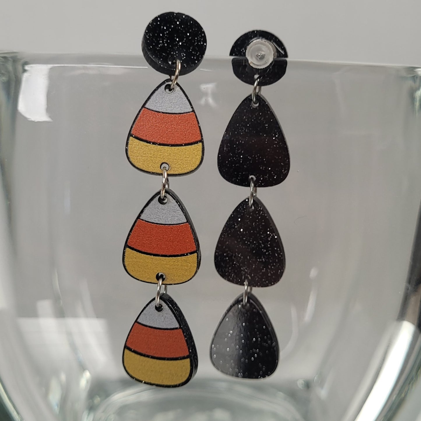 Pair of candy corn-themed earrings on a clear stand.