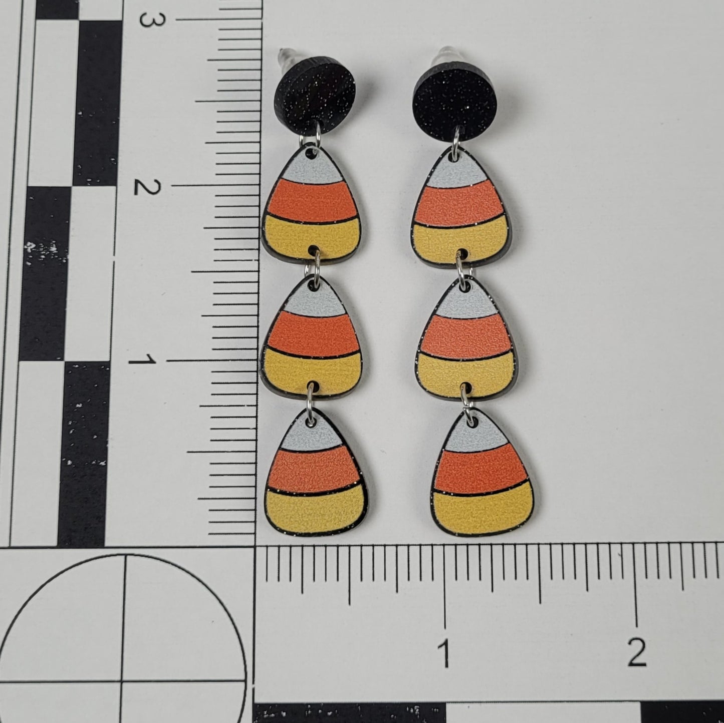 Candy corn-shaped earrings on a ruler for scale
