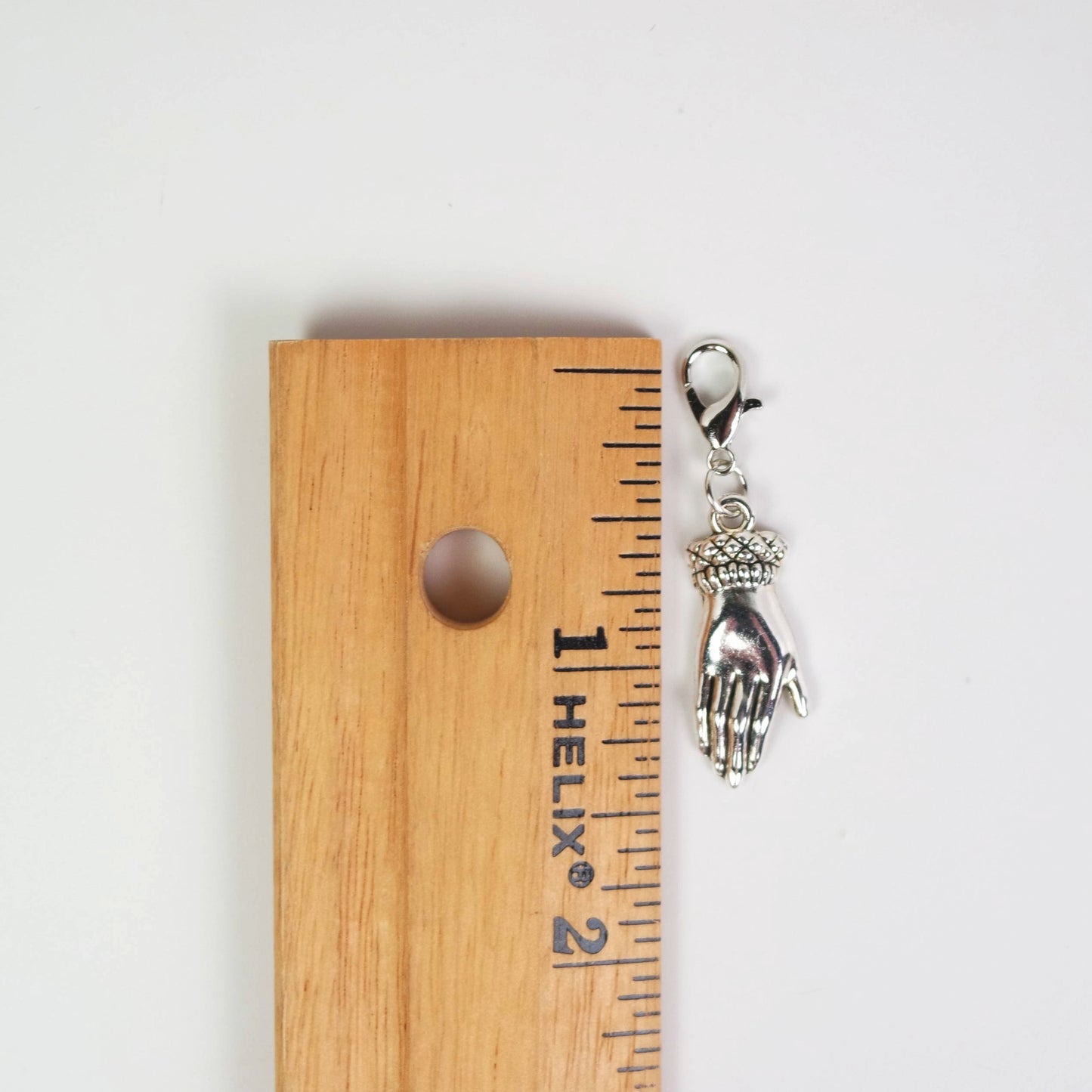 Silver hand-shaped keychain charm on a wooden ruler for scale