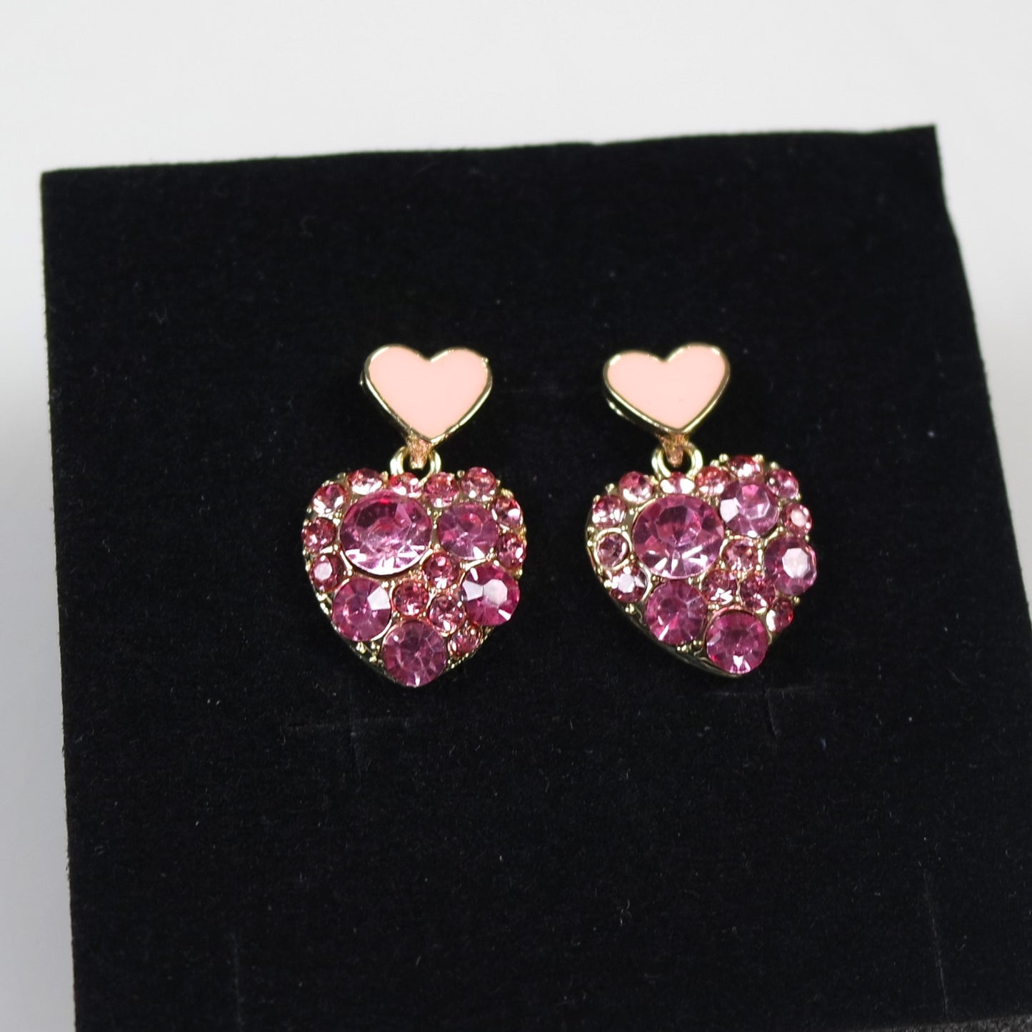 Heart-shaped earrings with pink gemstones on a black stand.