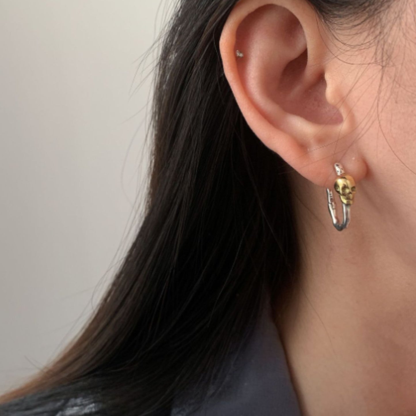 Close-up of an ear wearing a gold and silver hoop earring against a neutral background