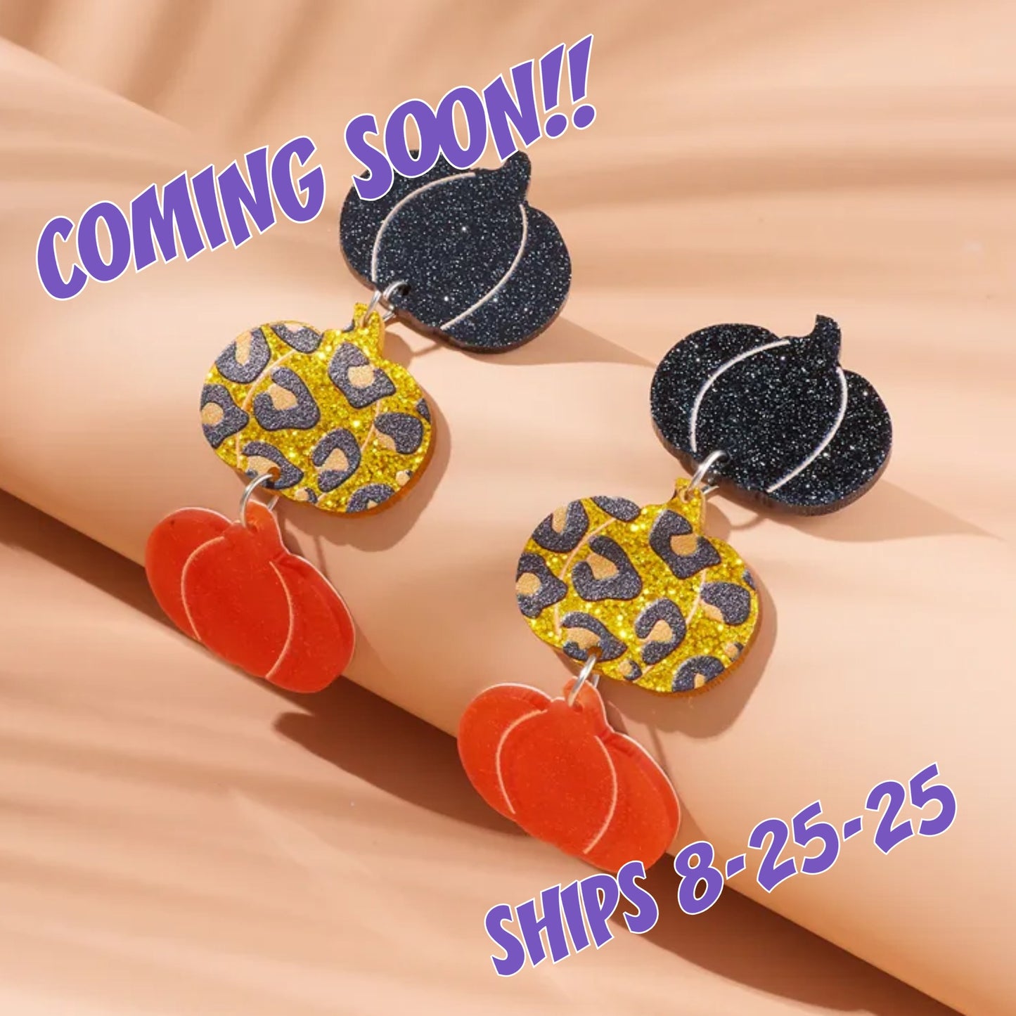 Halloween-themed earrings with pumpkins and glittery leaves on a beige background, with text indicating 'Coming Soon' and 'Ships 8-25-25'.