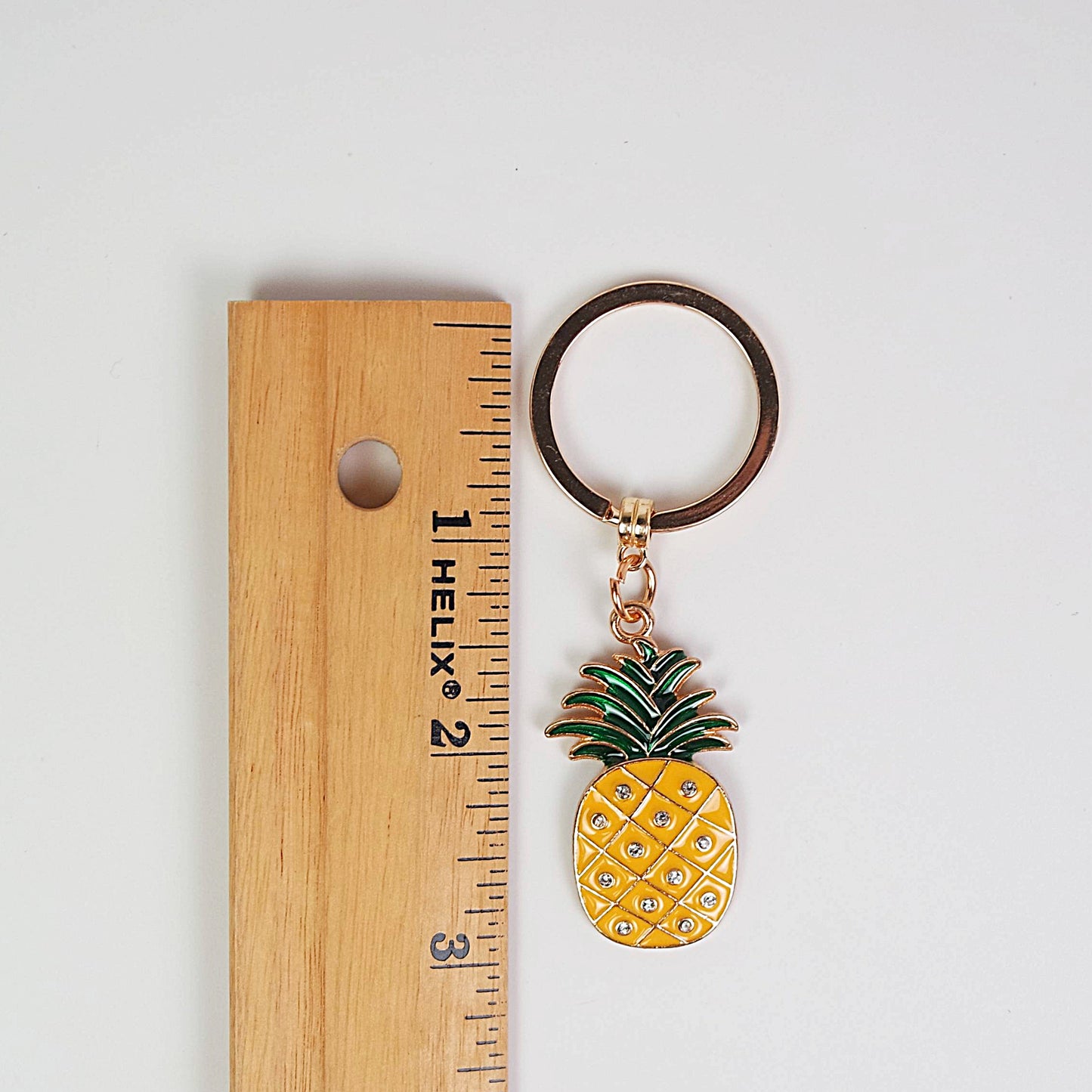 Pineapple-shaped keychain next to a ruler on a white background