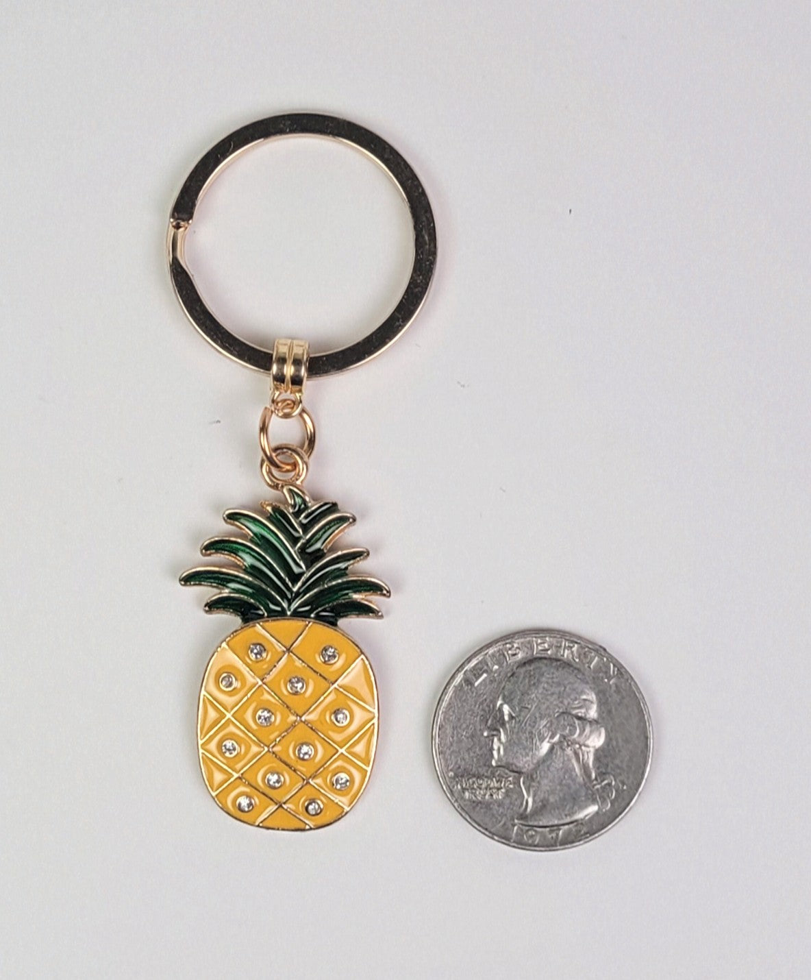 Pineapple-shaped keychain with a coin for size comparison on a white background