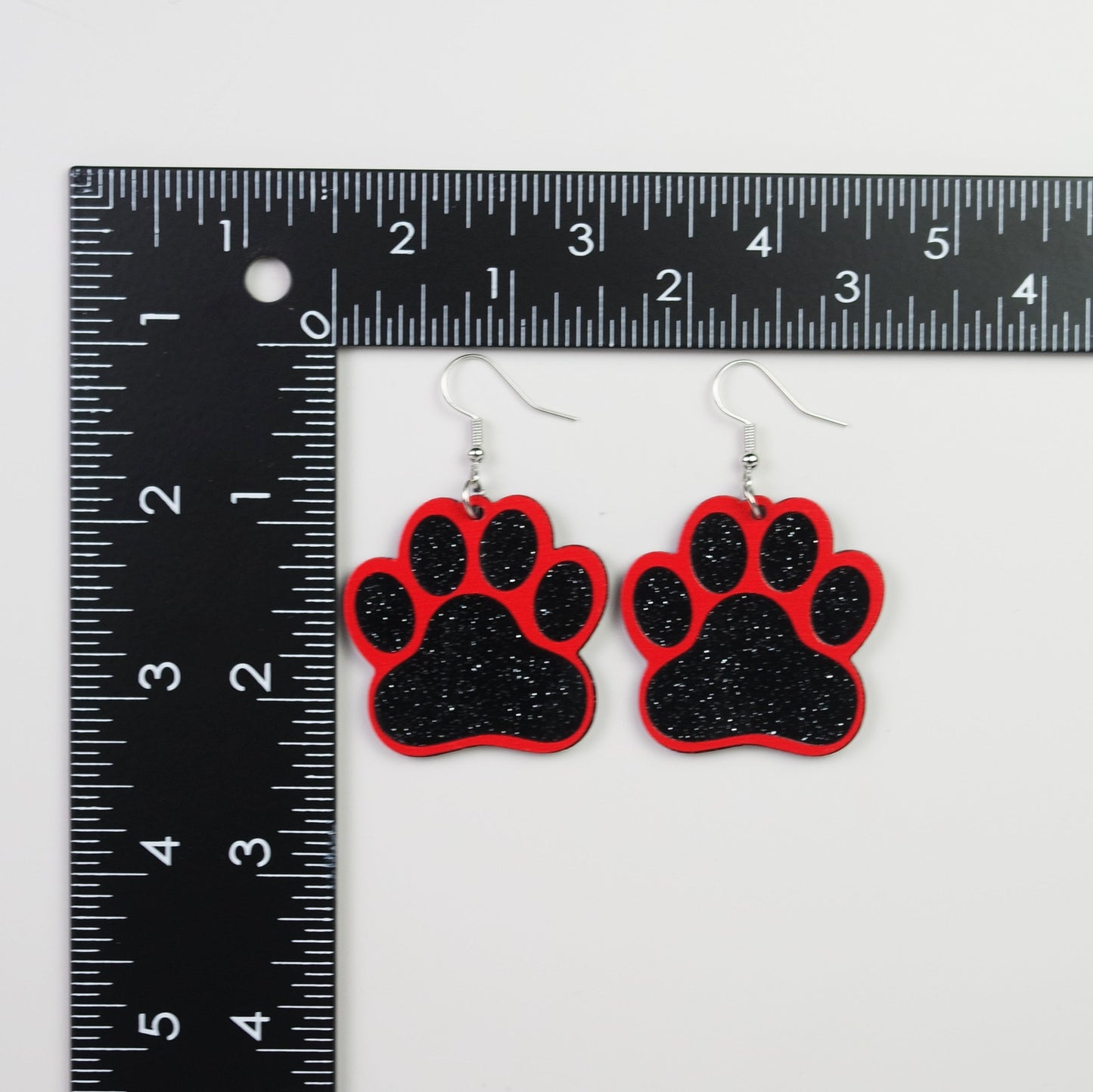 Red and black paw print earrings next to a ruler for size reference on a white background