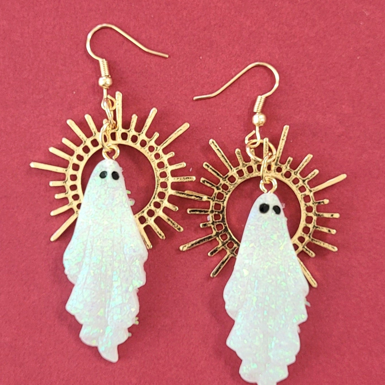 Gold and white ghost earrings on a pink background