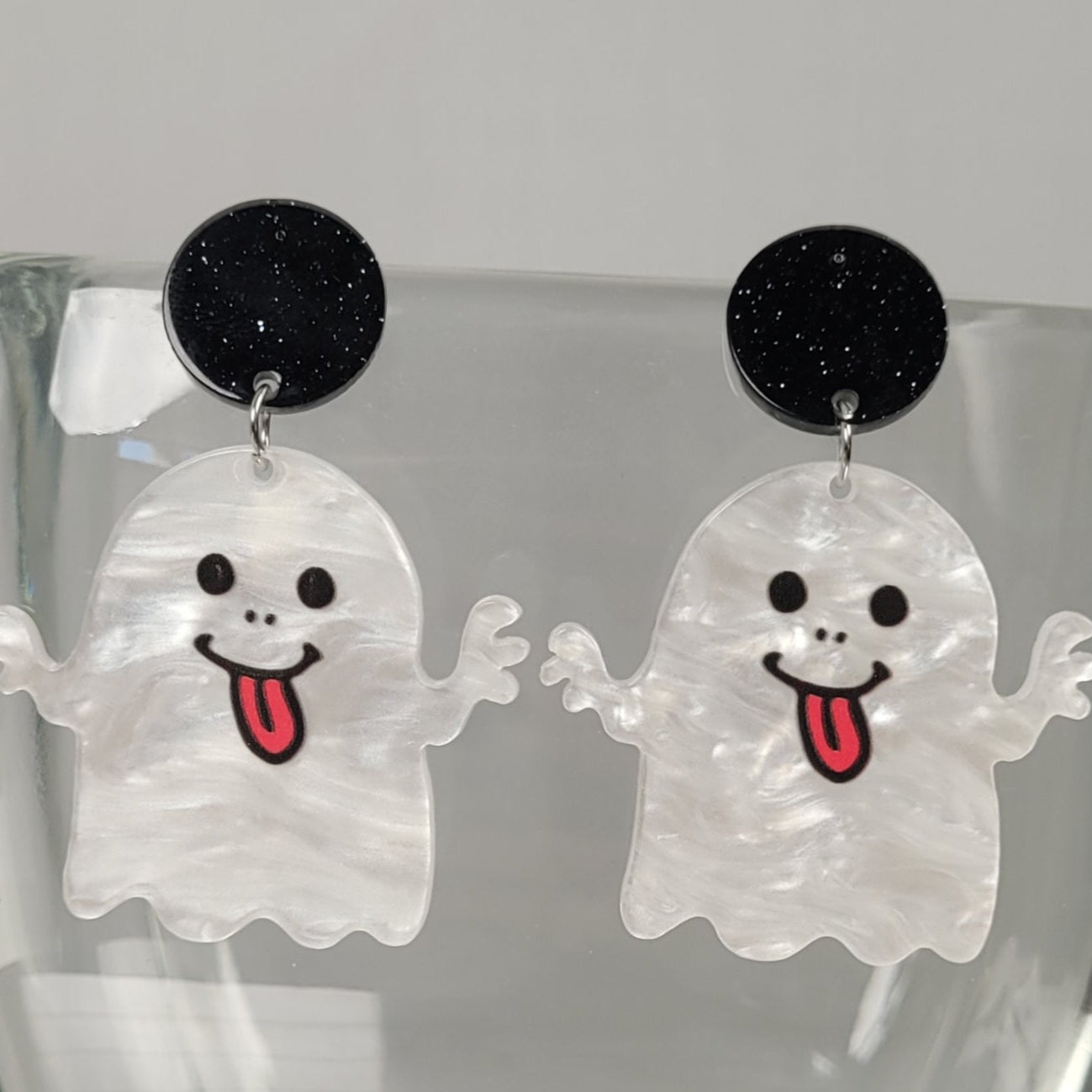 Ghost-shaped earrings with black accents on a glass surface