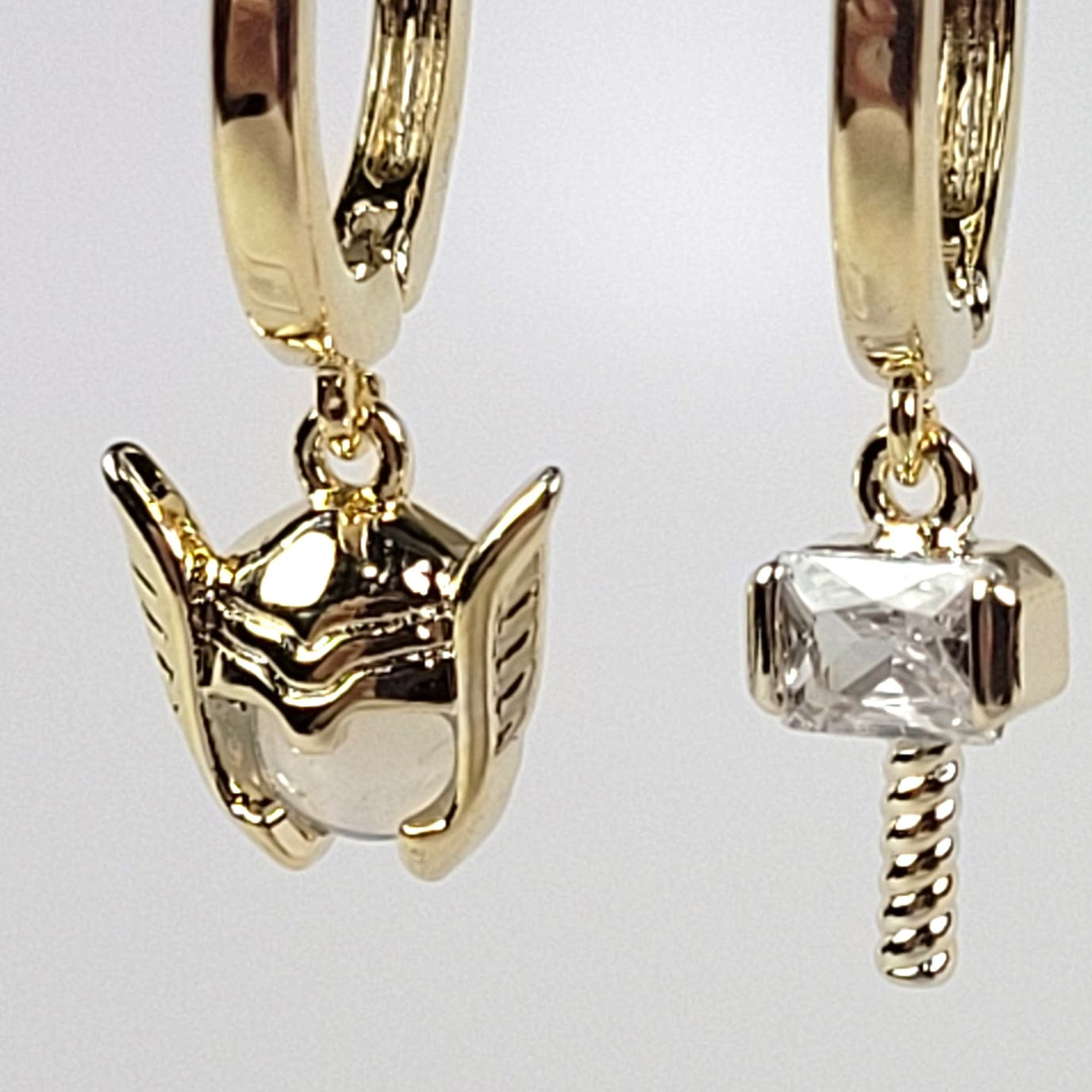 Gold hoop earrings with unique charms on a light gray background