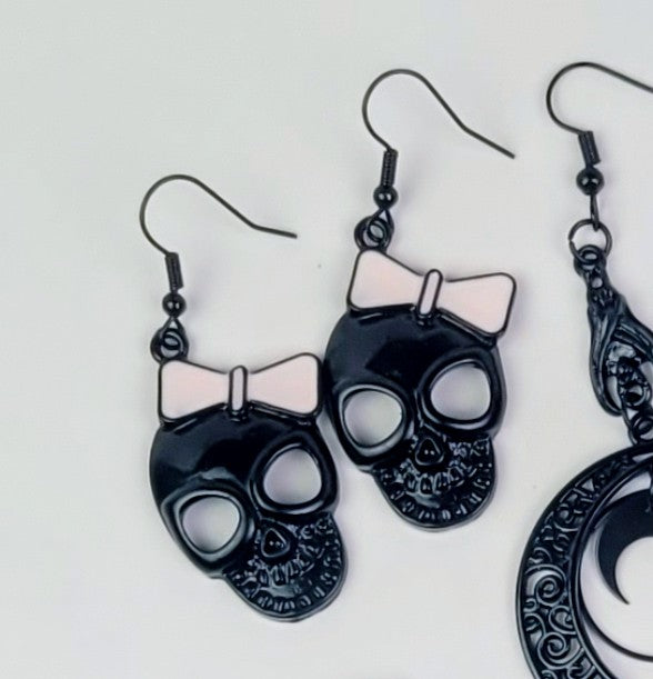 Black skull-shaped earrings with pink bows on a white background