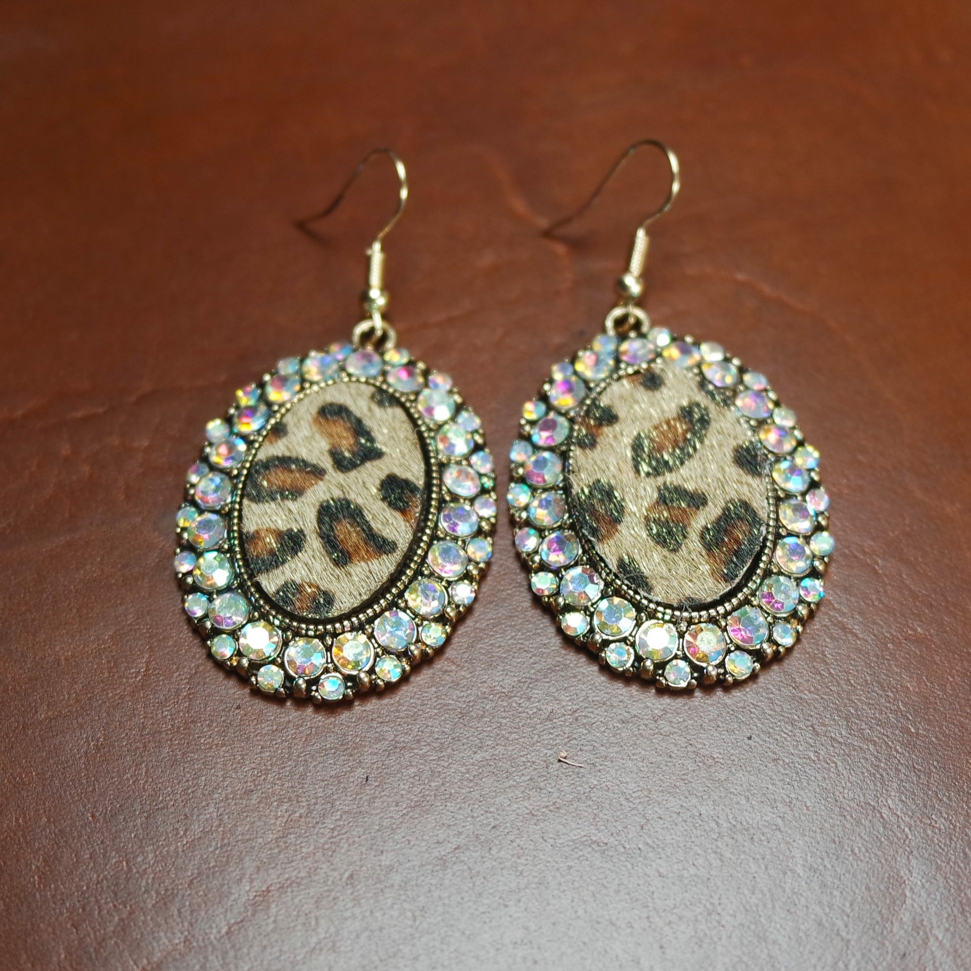 Leopard print earrings with rhinestone accents on a brown surface