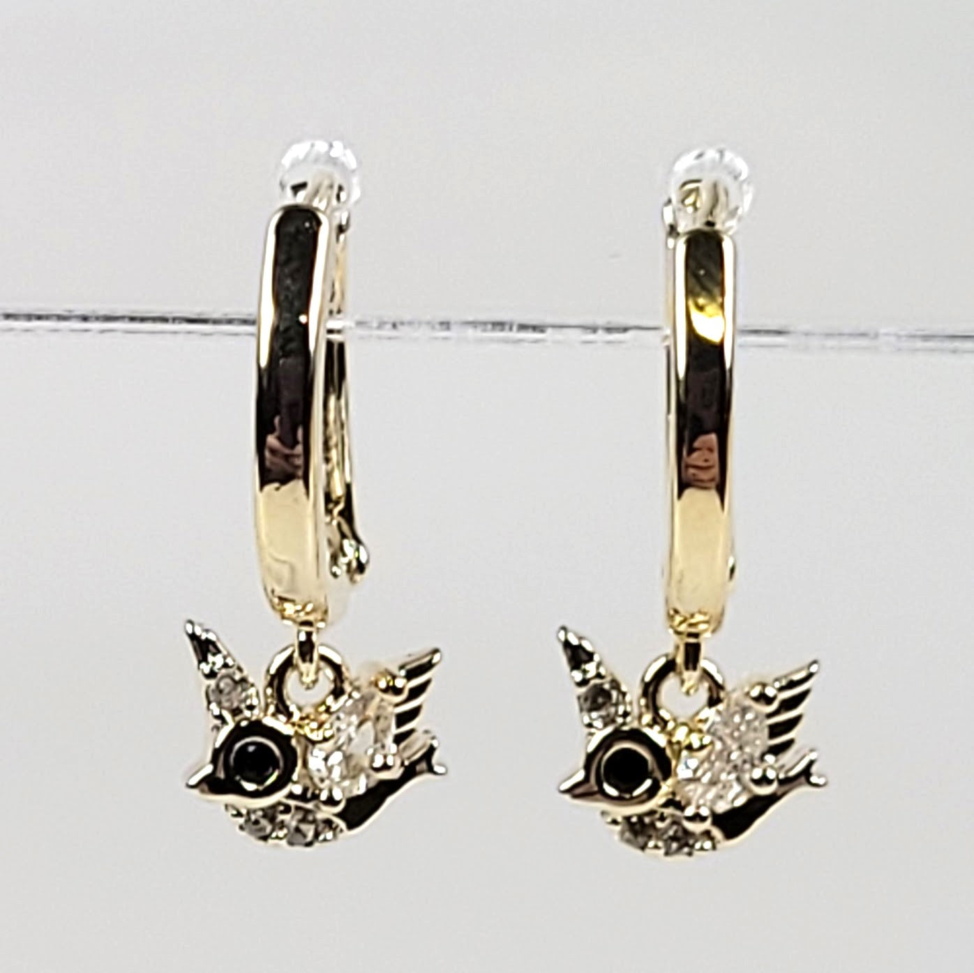 Gold hoop earrings with bird charms on a light gray background
