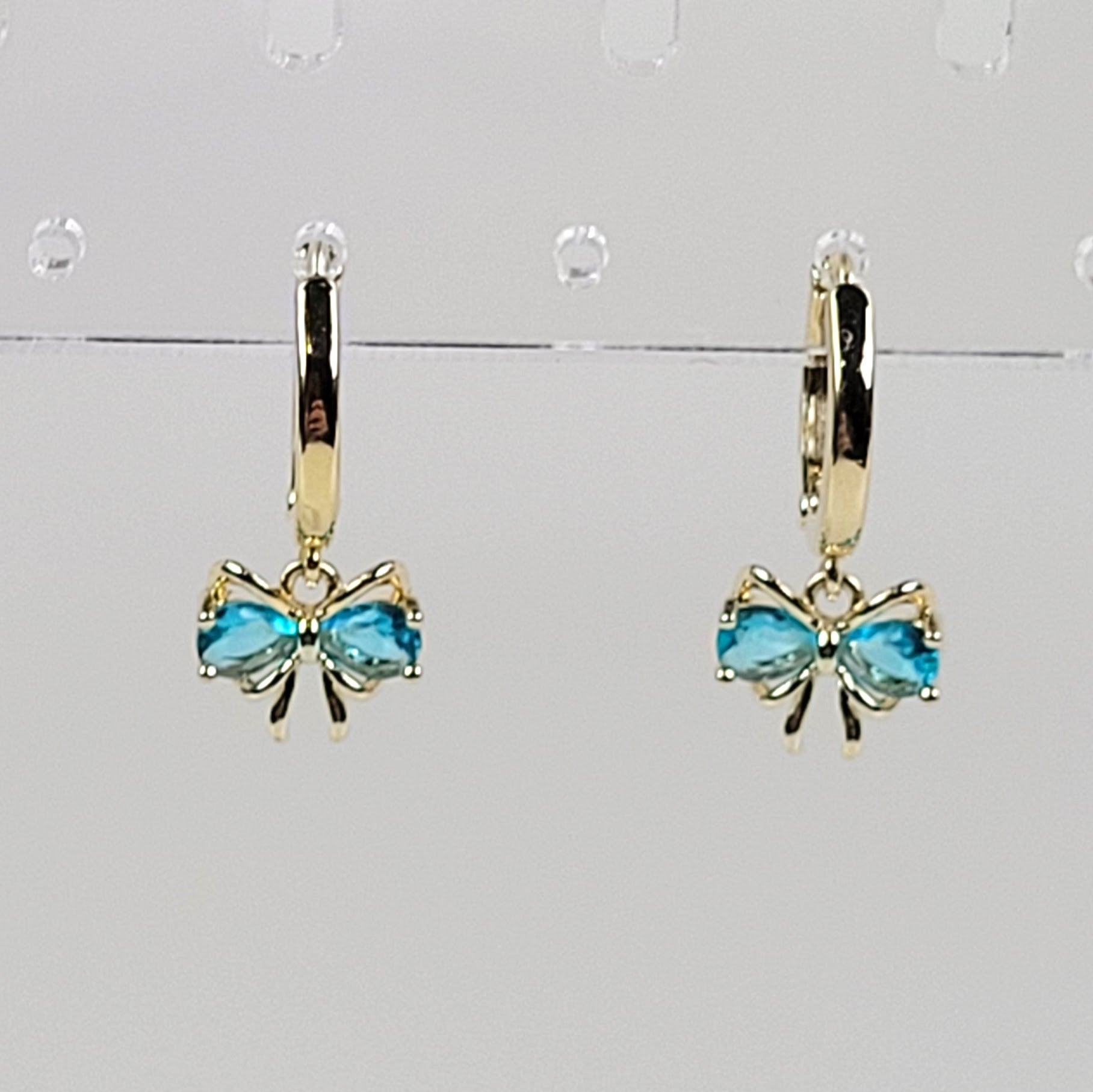 Gold bow earrings with blue gemstones on a gray background