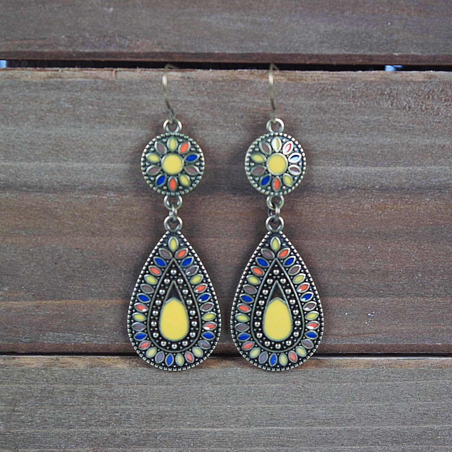 A pair of boho style dangle earrings with a disk to teardrop shape, featuring multicolor yellow enamel in an antique brass finish.