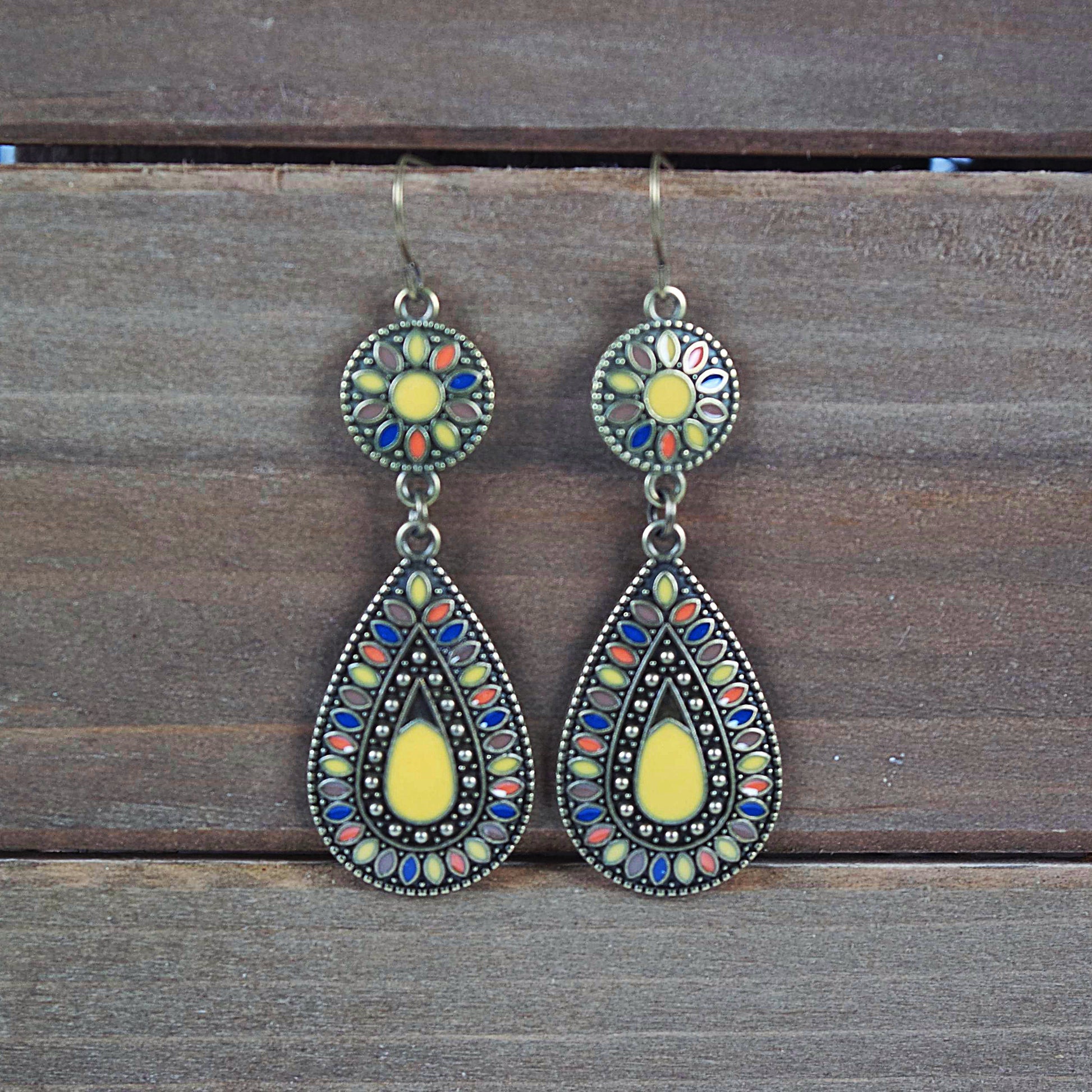 A pair of boho style dangle earrings with a disk to teardrop shape, featuring multicolor yellow enamel in an antique brass finish.