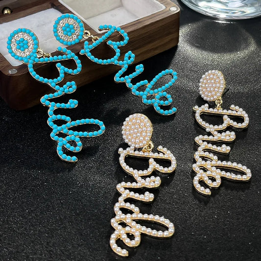 A pair of drop earrings designed with the word 'BRIDE' in capital letters, made of seed beads and rhinestones, displayed on a dark background.