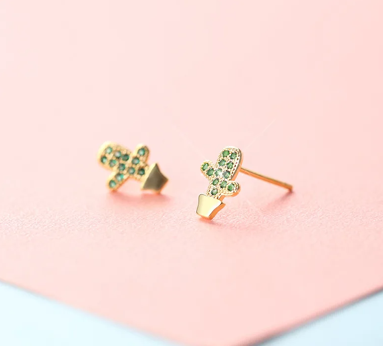 Gold earrings with green gemstones on a pink and blue gradient background