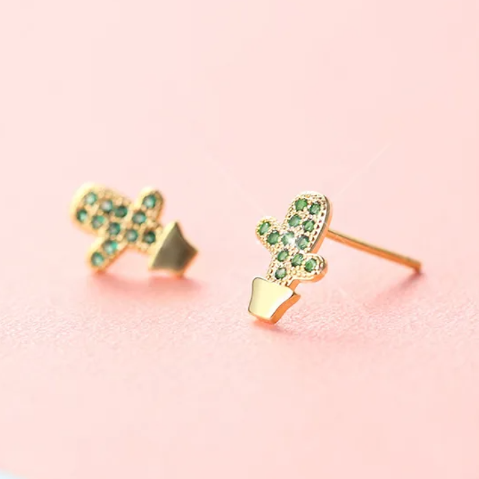 Gold earrings with green gemstones on a pink and blue gradient background
