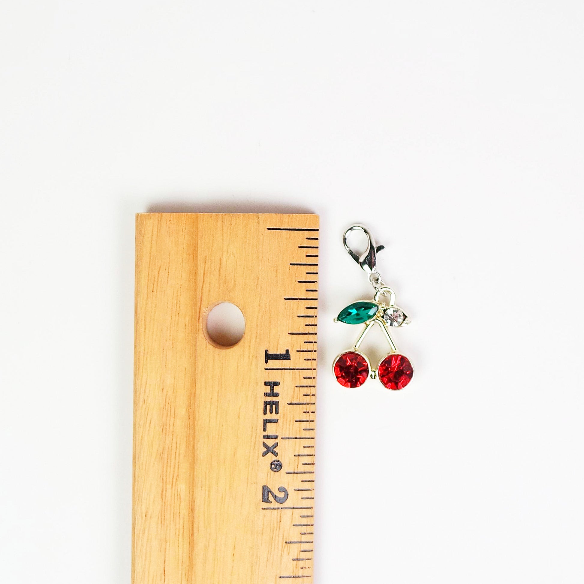Charm resembling cherries on a wooden ruler for scale