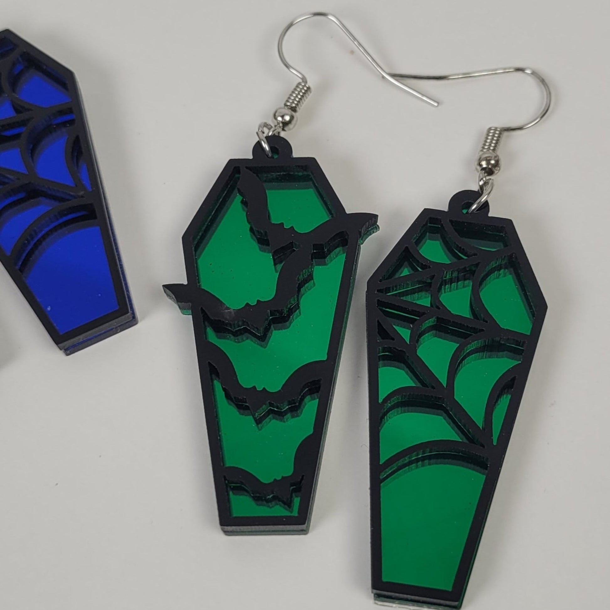 Coffin-shaped earrings with green and black design on a white background