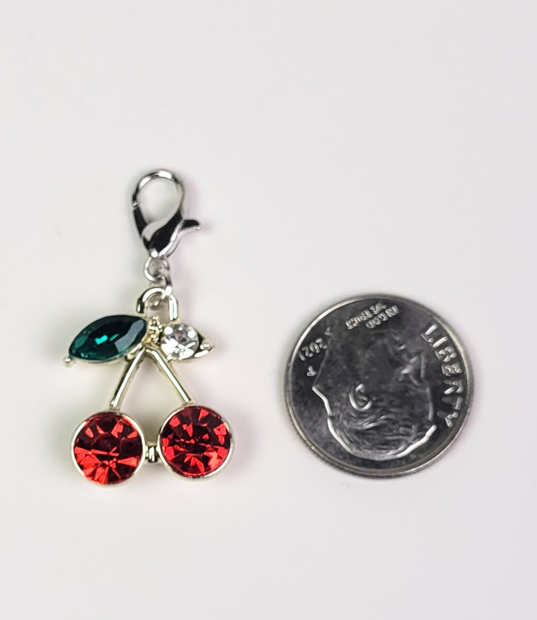 Charm with red and green gemstones on a white background Next to dime for size

