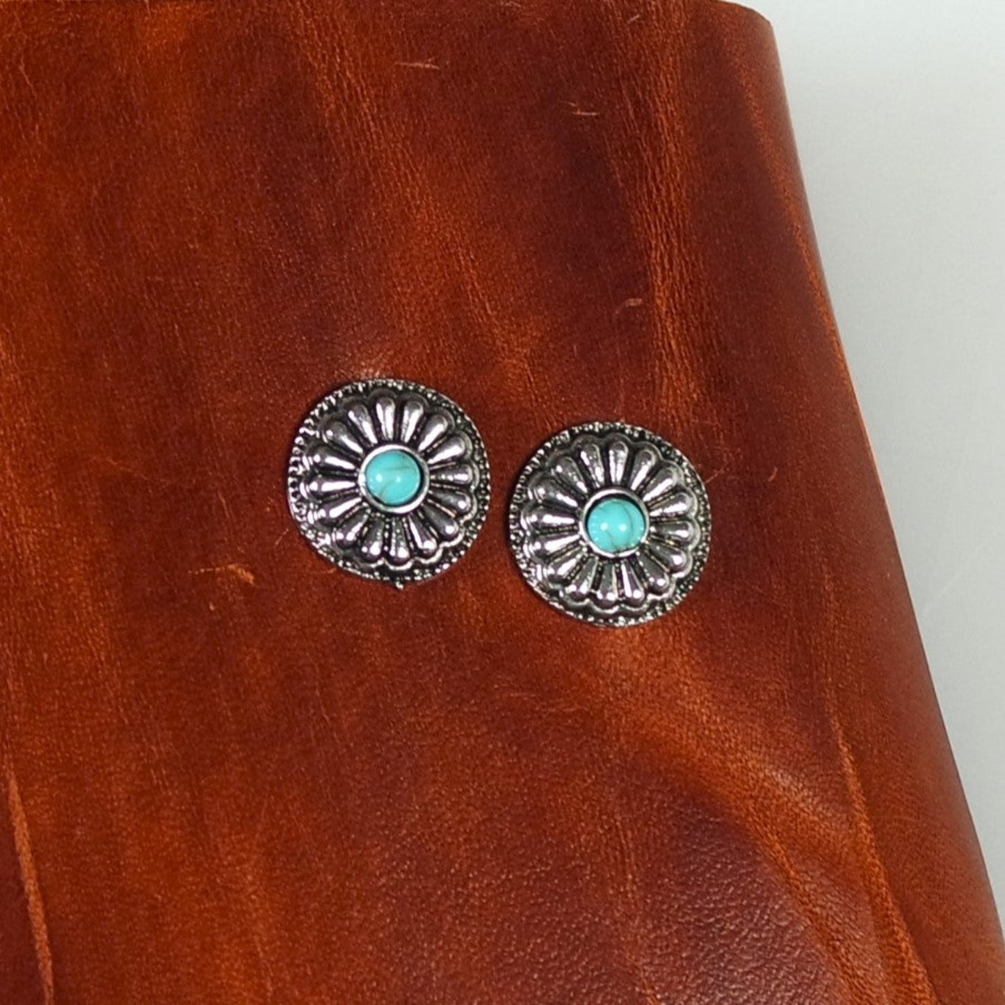 Silver earrings with turquoise stones on a brown leather surface