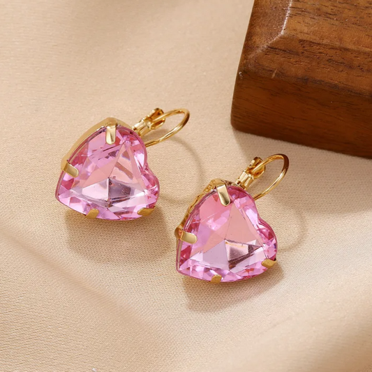 Pink heart-shaped earrings with gold accents on a beige surface.
