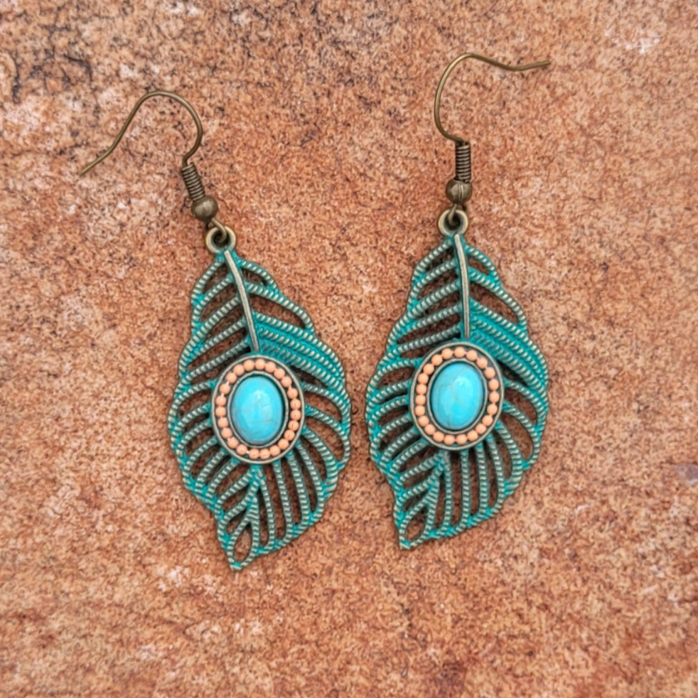 Pair of turquoise feather-shaped earrings on a brown surface