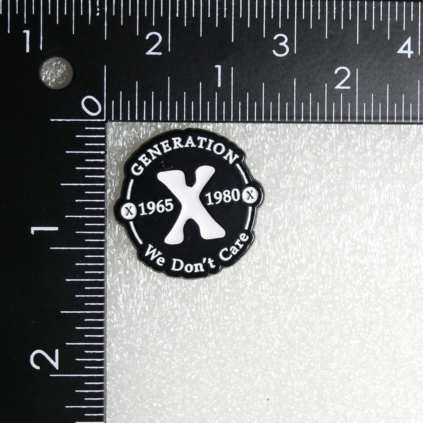 Black and white patch with 'Generation 1965 1980 We Don't Care' text and design, measured against a ruler.