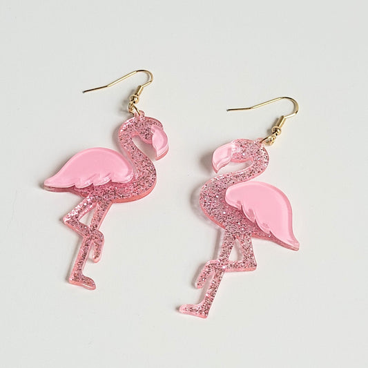A pair of pink acrylic dangle earrings in the shape of flamingos with glitter finish.