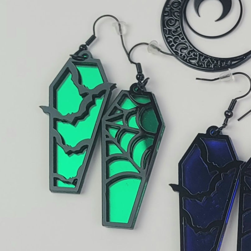 Green coffin-shaped earrings with spider web design on a white background